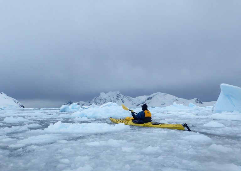 A solo kayaker paddling through the sea ice in Antarctica.