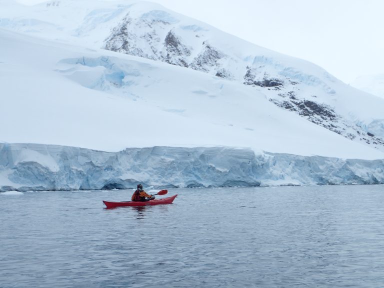 A solo paddler kayaking in Antarctica along a glacier face.